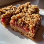 Three squares of golden brown Rhubarb Oat Bars showing a thick oat base and crumbly topping over a bright red rhubarb filling.