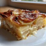 A close-up of a thick slice of savory Rhubarb-Potato Gratin with Gruyère showing layered potatoes and a browned, cheesy top.