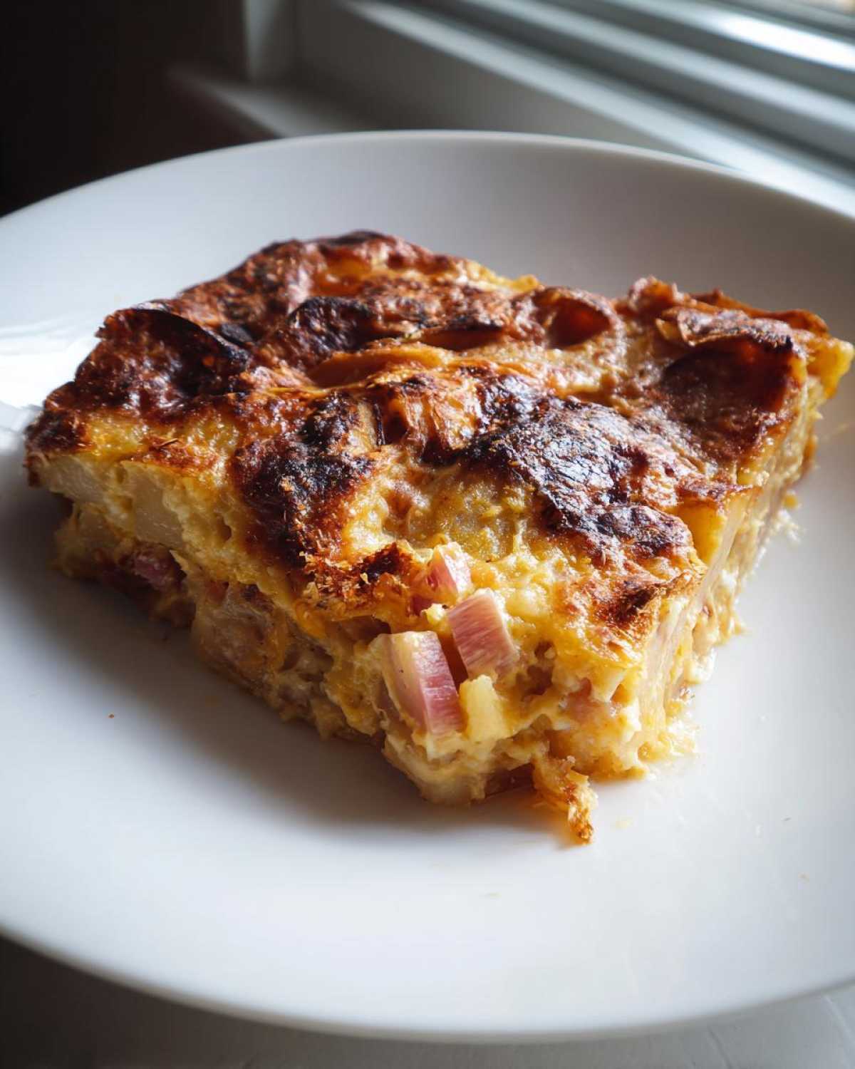A golden-brown slice of savory Rhubarb-Potato Gratin with Gruyère served on a white plate.