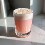 A tall, pink Rhubarb Rose Ramos Gin Fizz cocktail topped with thick white foam and pink/gold sprinkles.