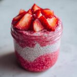 Close-up of layered Rhubarb Strawberry Chia Pudding topped with fresh sliced strawberries in a glass jar.