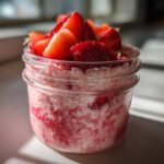 Close-up of Rhubarb Strawberry Chia Pudding layered with fruit puree and topped with fresh sliced strawberries in a mason jar.