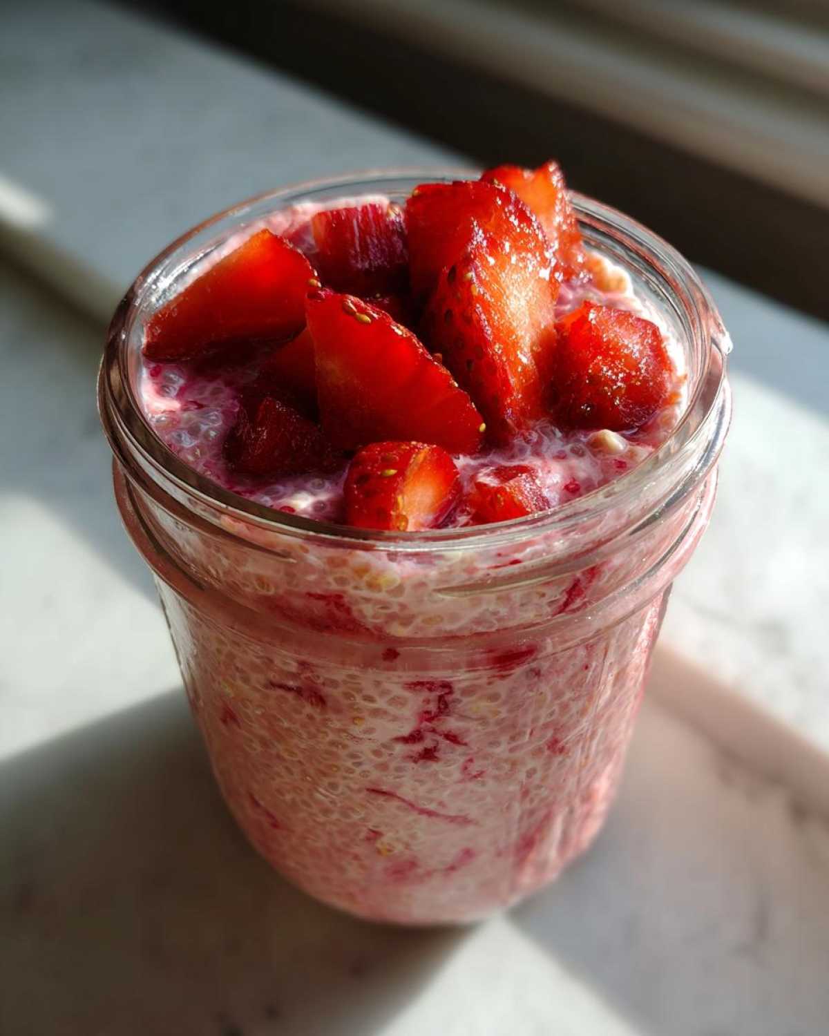 Close-up of Rhubarb Strawberry Chia Pudding topped with fresh sliced strawberries in a glass jar.