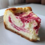 Close-up of a creamy slice of Rhubarb and White Chocolate Cheesecake with pink swirls on a white plate.