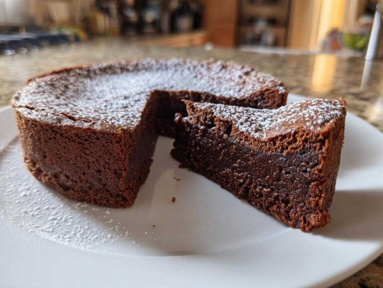 A rich, dark flourless chocolate torte with a slice cut out, dusted lightly with powdered sugar.