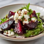 Close-up of vibrant Roasted Beet & Goat Cheese Salad featuring dark red beets, crumbled goat cheese, and arugula drizzled with balsamic glaze.