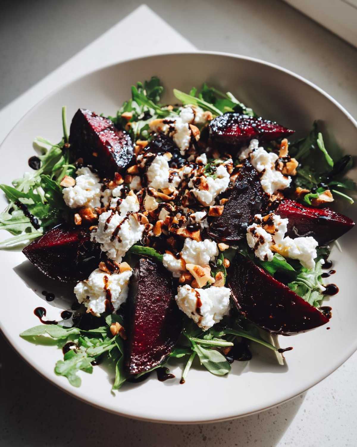 A close-up of a vibrant Roasted Beet & Goat Cheese Salad featuring dark roasted beets, crumbled white goat cheese, and a balsamic glaze over arugula.