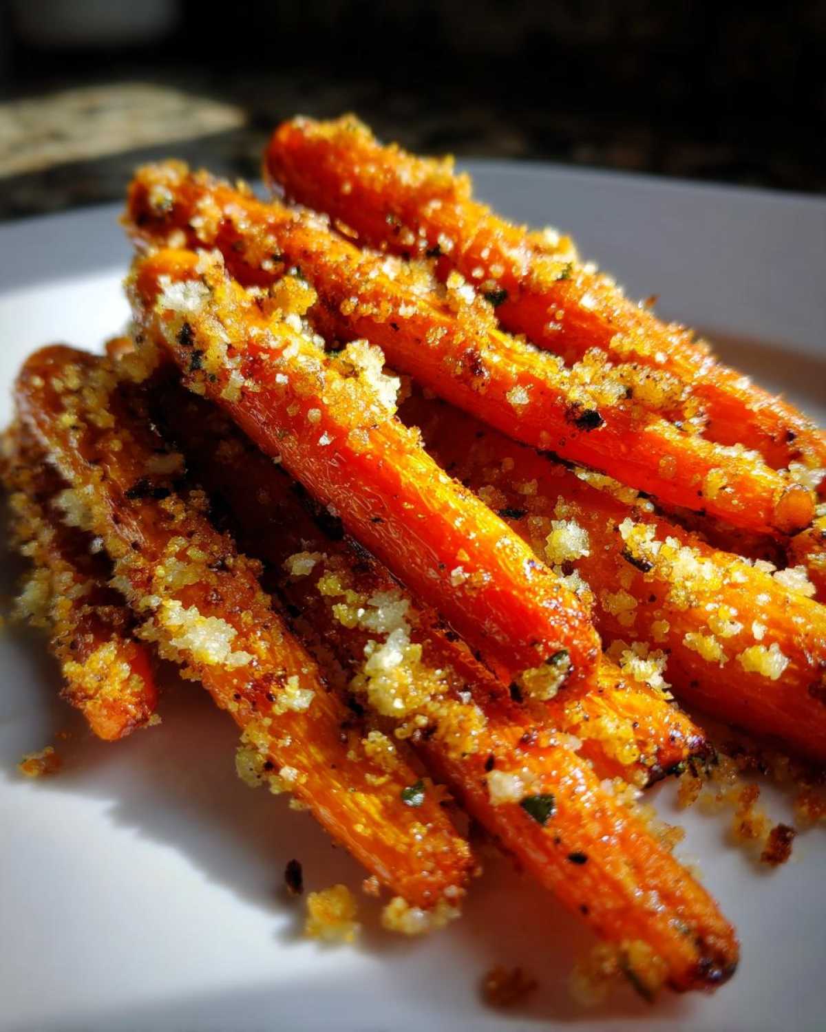 Close-up of bright orange Roasted Parmesan Garlic Carrots piled on a white plate, coated in crispy topping.