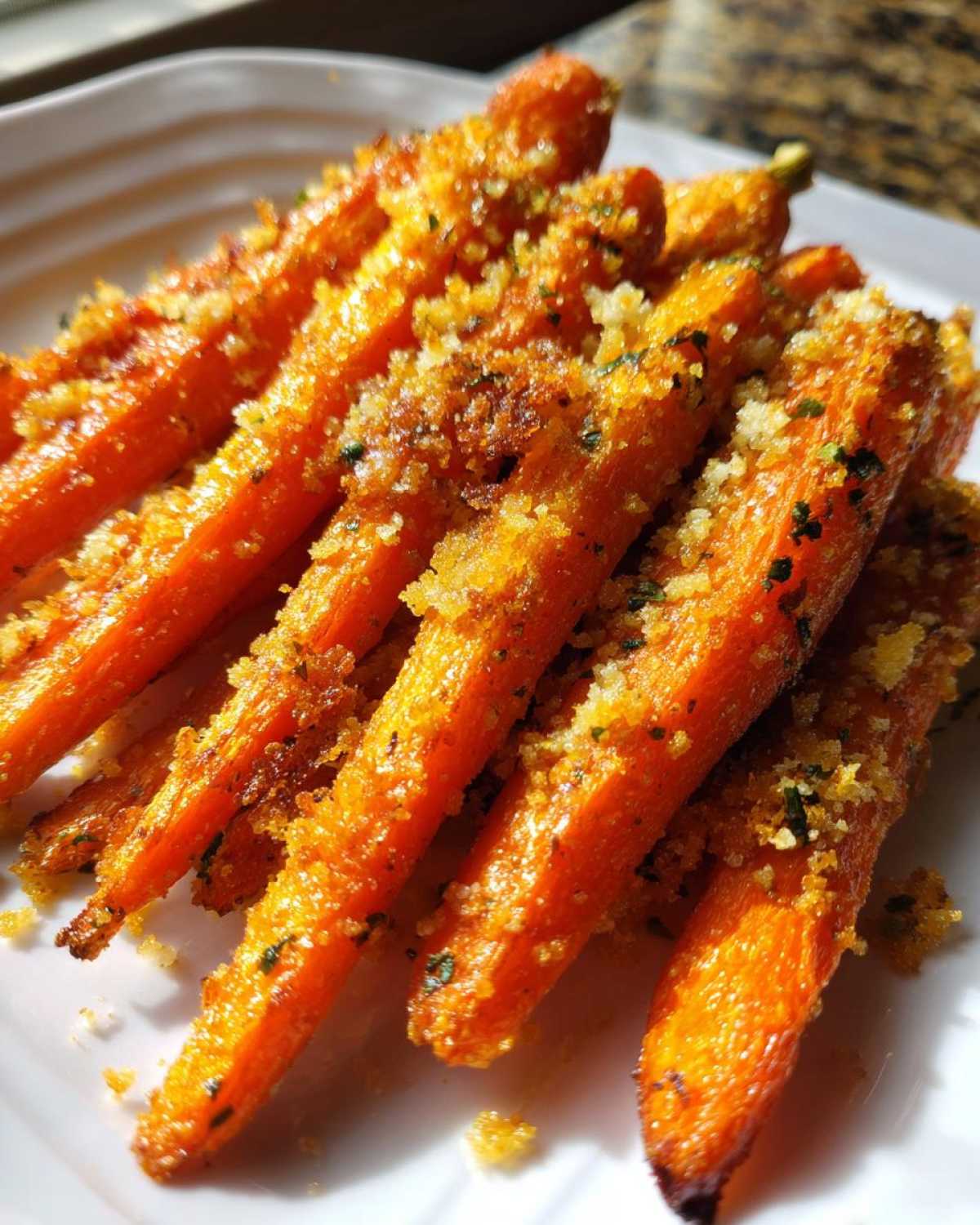 Close-up of bright orange Roasted Parmesan Garlic Carrots piled on a white plate, coated in crispy breadcrumbs and herbs.