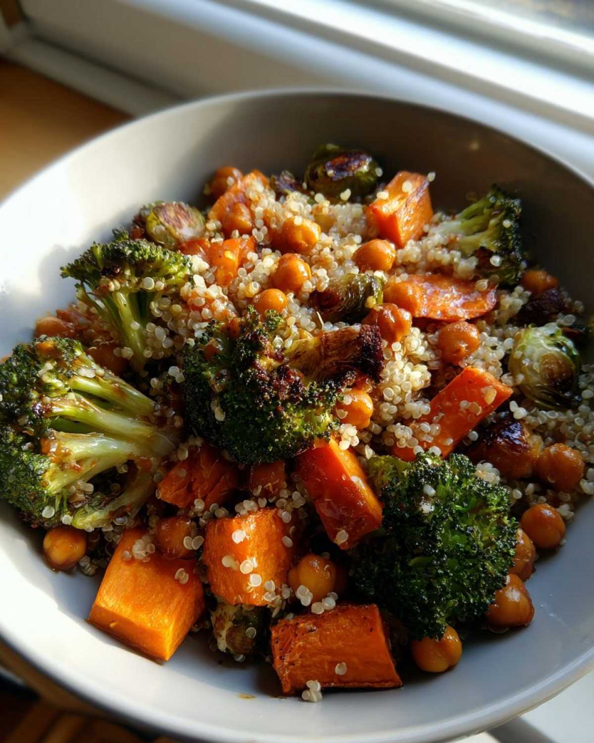 A close-up of a bowl containing Roasted Vegetable Quinoa Salad with roasted broccoli, sweet potato chunks, chickpeas, and Brussels sprouts.