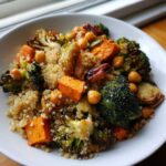 A close-up of a white bowl filled with Roasted Vegetable Quinoa Salad, featuring roasted broccoli, sweet potatoes, chickpeas, and Brussels sprouts.