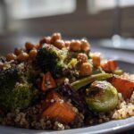 A close-up, appetizing shot of Roasted Vegetable Quinoa Salad featuring roasted broccoli, sweet potatoes, chickpeas, and Brussels sprouts.