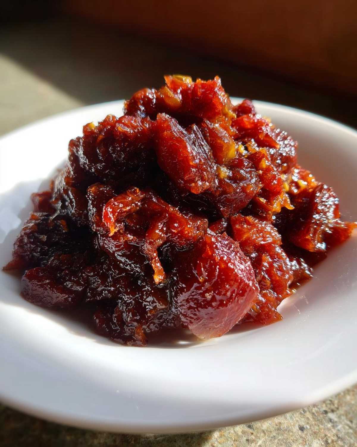 A close-up of rich, dark red Savory Rhubarb Chutney with Dates piled high in a small white bowl.