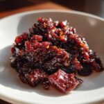 Close-up of a dollop of dark, glossy Savory Rhubarb Chutney with Dates served on a white dish.