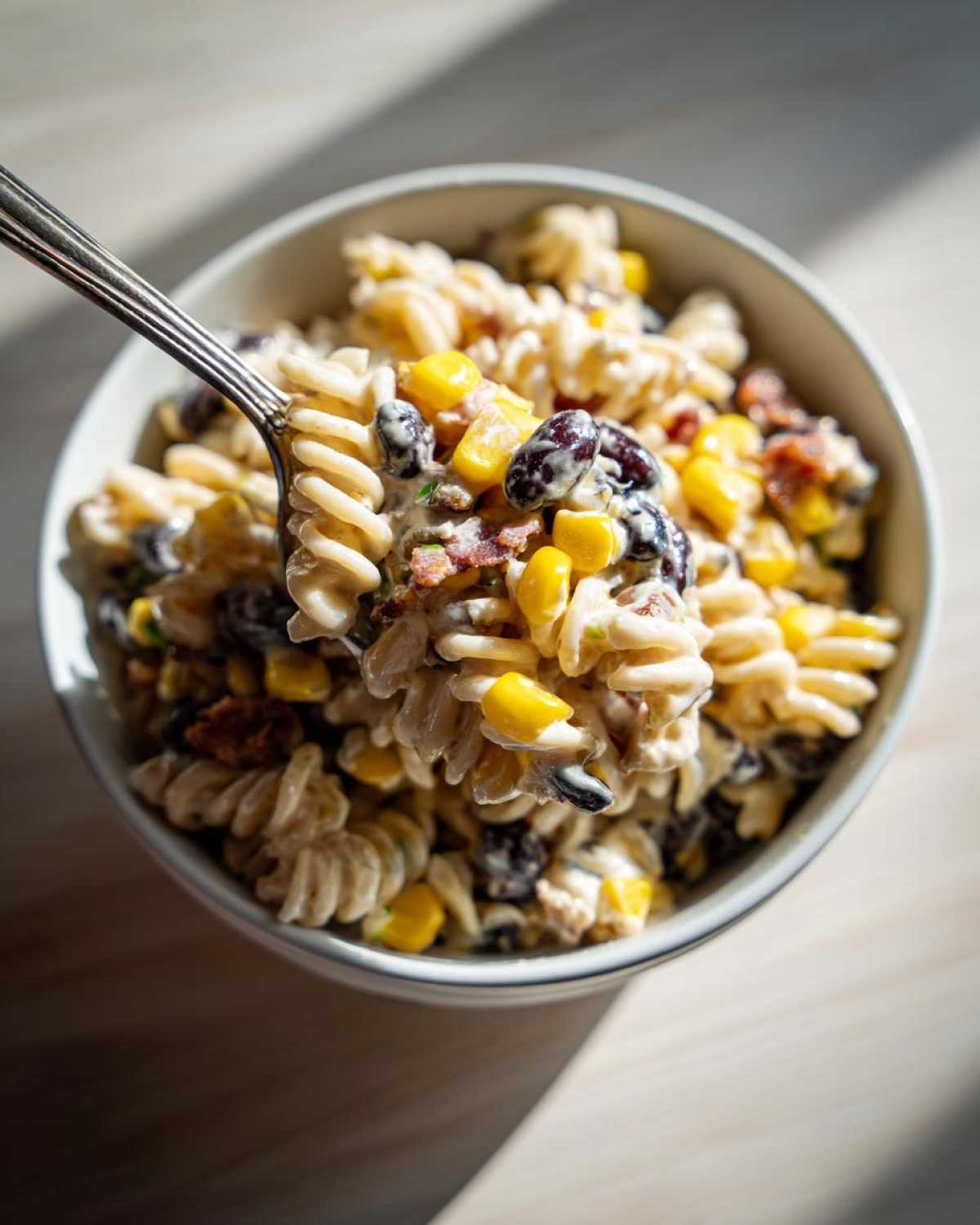 A fork lifting a creamy scoop of Cowboy Pasta Salad featuring rotini pasta, corn kernels, black beans, and bacon bits.