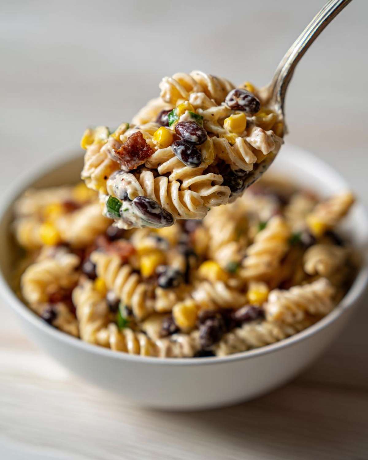 A spoonful of creamy Cowboy Pasta Salad featuring rotini pasta, black beans, and corn being lifted from a white bowl.