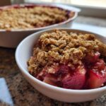 Close-up of a serving of warm Gluten-Free Rhubarb Crisp with a golden oat topping in a white bowl.