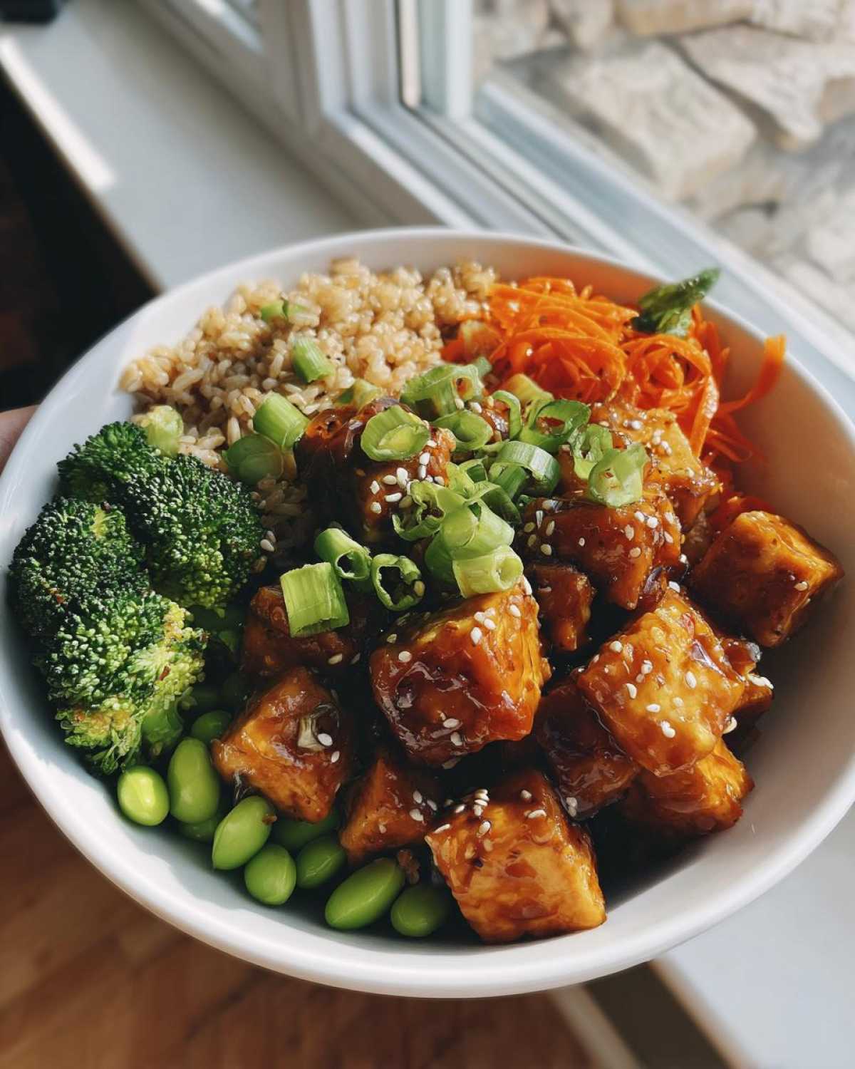 A close-up of a vibrant Sesame Ginger Tofu Bowls featuring glazed tofu, brown rice, broccoli, edamame, and shredded carrots.
