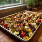A full sheet pan of Sheet Pan Greek Chicken & Veggies topped with feta, olives, and herbs.
