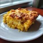 A close-up of a golden-brown slice of moist gluten-free squash casserole served on a white plate.
