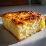A square slice of creamy hashbrown casserole with a deeply browned, cheesy top, served on a white plate.