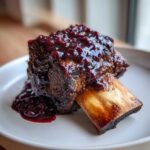 A single, tender Slow-Roasted Rhubarb Short Ribs piece covered in a rich, dark red rhubarb glaze, served on a white plate.