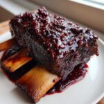 Close-up of tender Slow-Roasted Rhubarb Short Ribs covered in a thick, glossy, dark red rhubarb glaze.