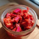 Close-up of bright red, chopped rhubarb pieces coated in seasoning inside a glass jar of Small-Batch Rhubarb Kimchi.