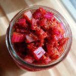 Overhead view of vibrant red Small-Batch Rhubarb Kimchi packed tightly in a clear glass jar.