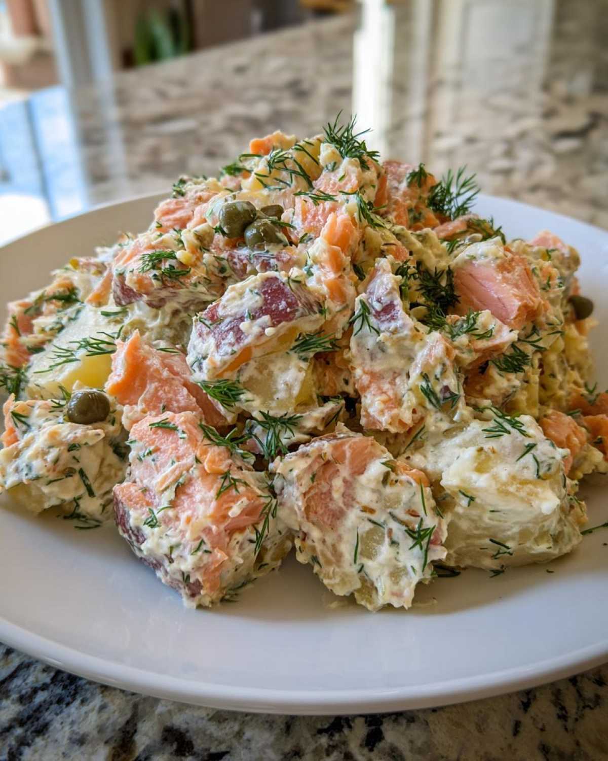 A mound of creamy smoked salmon potato salad recipe featuring chunks of red-skinned potatoes, pink salmon, and fresh dill.