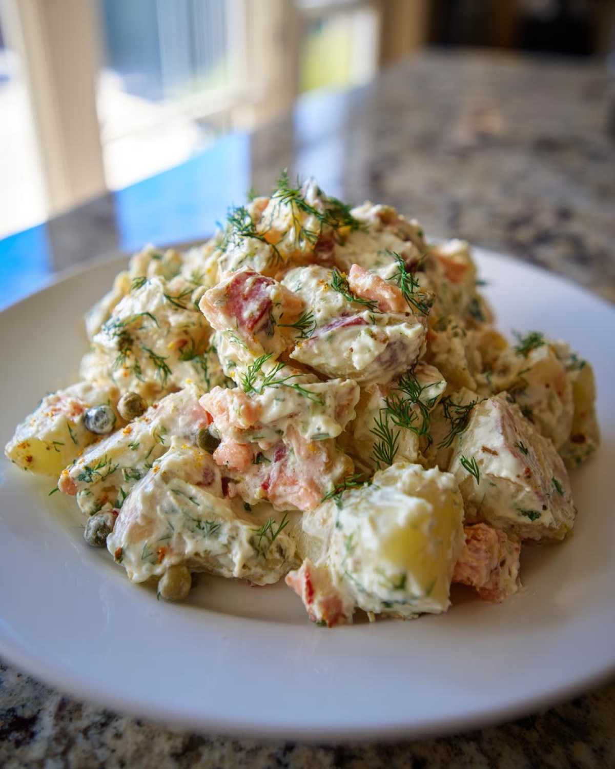 A close-up of a creamy smoked salmon potato salad recipe served on a white plate, garnished with fresh dill.