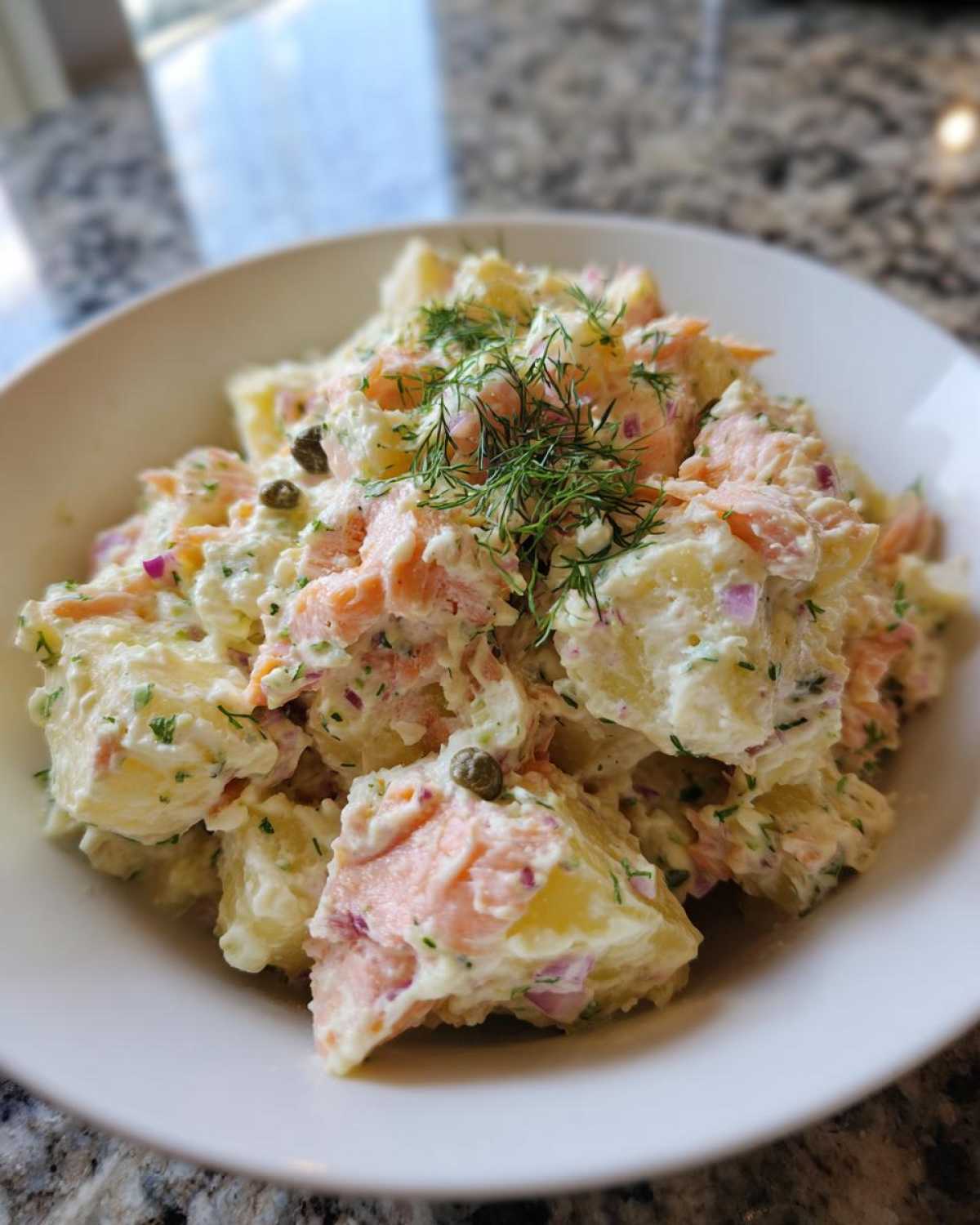 Close-up of a creamy smoked salmon potato salad recipe, garnished with fresh dill and capers.