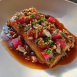 A fillet of Smoked Trout with Brown Butter served with bright pink rhubarb cubes, nuts, and parsley.