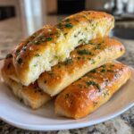 A stack of soft, golden garlic butter breadsticks topped with fresh parsley and coarse salt.