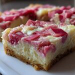 A close-up of a thick, baked square featuring a graham cracker crust topped with creamy filling and bright pink chunks of rhubarb in these Sour Cream Rhubarb Squares with Lemon.