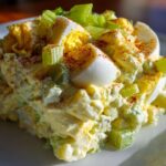 A close-up, featured image of a scoop of creamy Southern Potato Salad topped with sliced hard-boiled eggs and chopped celery.