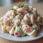 A mound of creamy Southern Shrimp Pasta Salad featuring elbow macaroni, pink shrimp, red onion, and celery, garnished with fresh herbs.