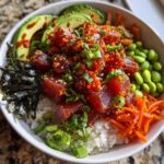 A vibrant bowl of Spicy Tuna Poke Bowls featuring marinated tuna, rice, avocado slices, edamame, and shredded carrots.