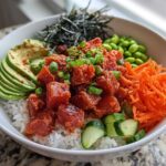 A vibrant bowl featuring Spicy Tuna Poke Bowls over rice, topped with avocado, carrots, edamame, and nori.