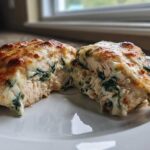 A close-up of Spinach & Artichoke Stuffed Chicken cut in half, showing the creamy filling inside and melted, browned cheese topping.