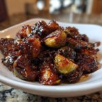 Close-up of roasted Brussels sprouts coated in a thick, dark Sticky Brussels Sprouts Glaze served in a white bowl.