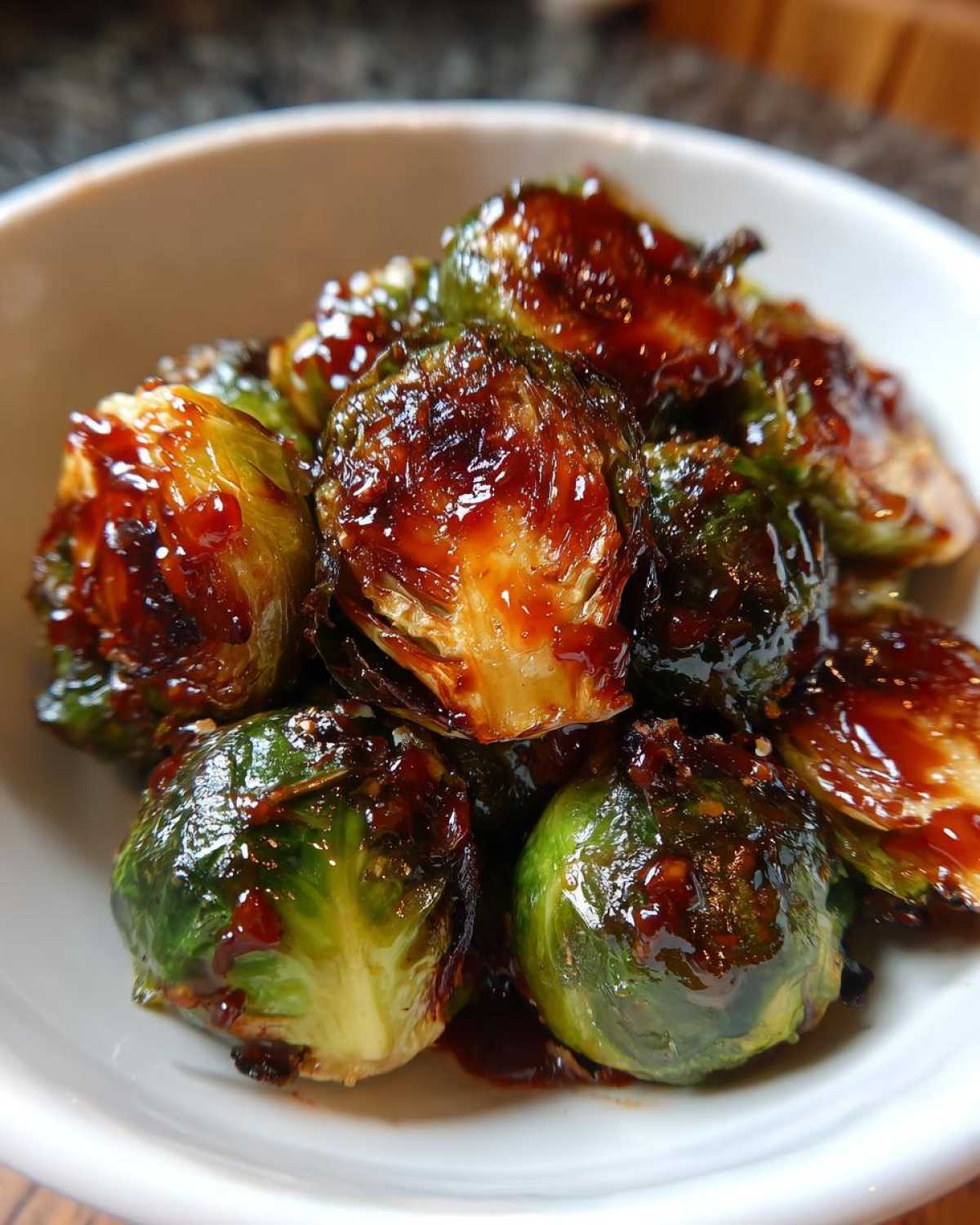 Close-up of roasted Brussels sprouts coated in a thick, shiny Sticky Brussels Sprouts Glaze served in a white bowl.