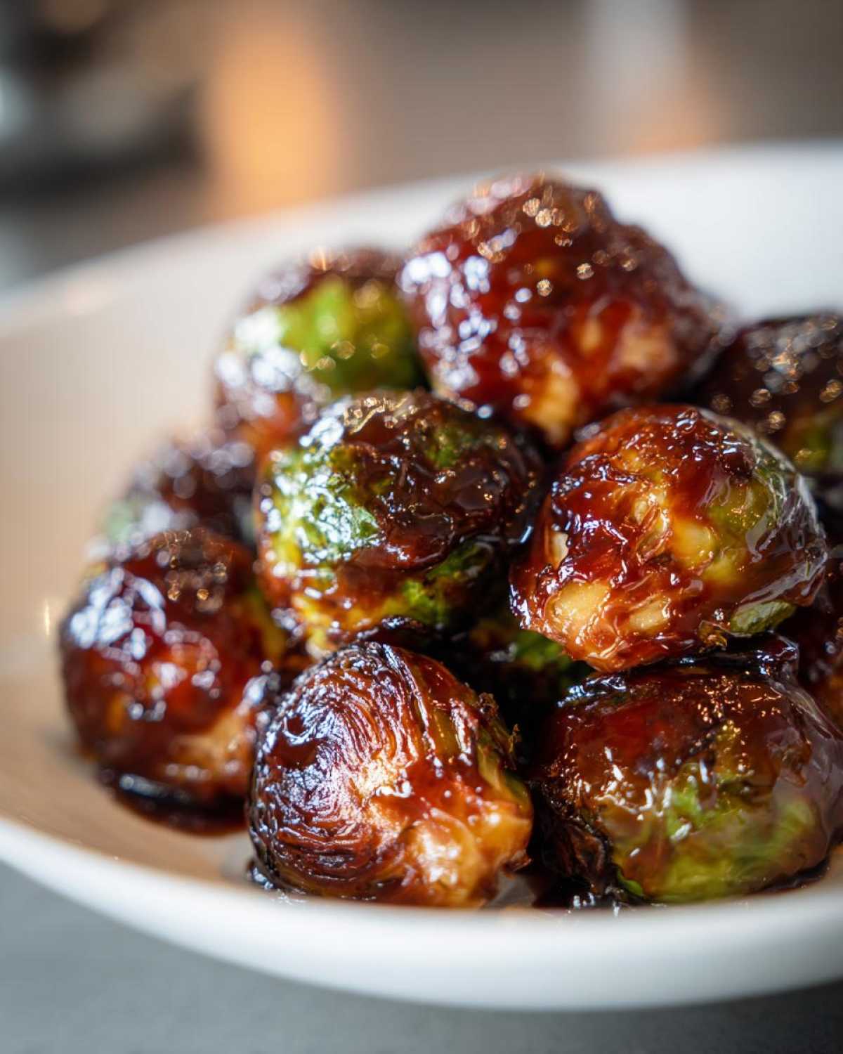 Close-up of roasted Brussels sprouts coated in a thick, shiny Sticky Brussels Sprouts Glaze served in a white bowl.