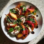 A close-up of a Stone Fruit Caprese Salad featuring sliced peaches, fresh mozzarella, and basil drizzled with balsamic glaze.