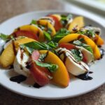 Close-up of a beautiful Stone Fruit Caprese Salad featuring peach slices, fresh mozzarella, and basil drizzled with balsamic glaze.