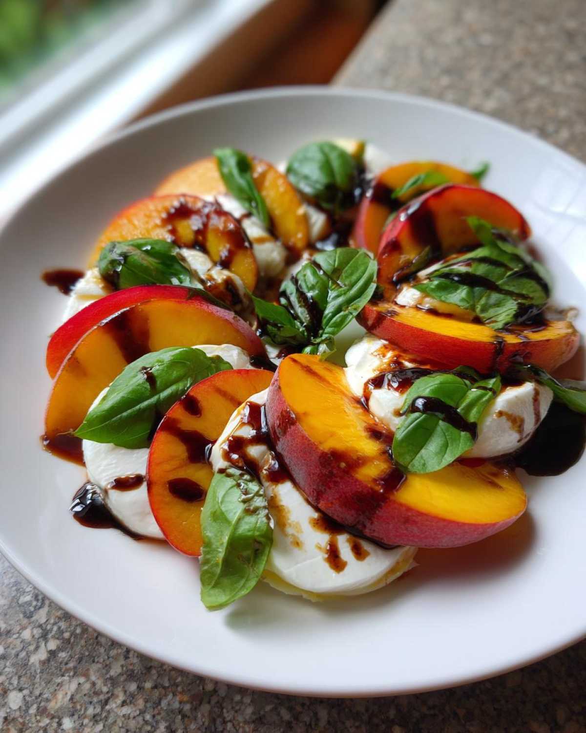 A vibrant Stone Fruit Caprese Salad featuring sliced peaches, fresh mozzarella, basil leaves, and a drizzle of balsamic glaze.