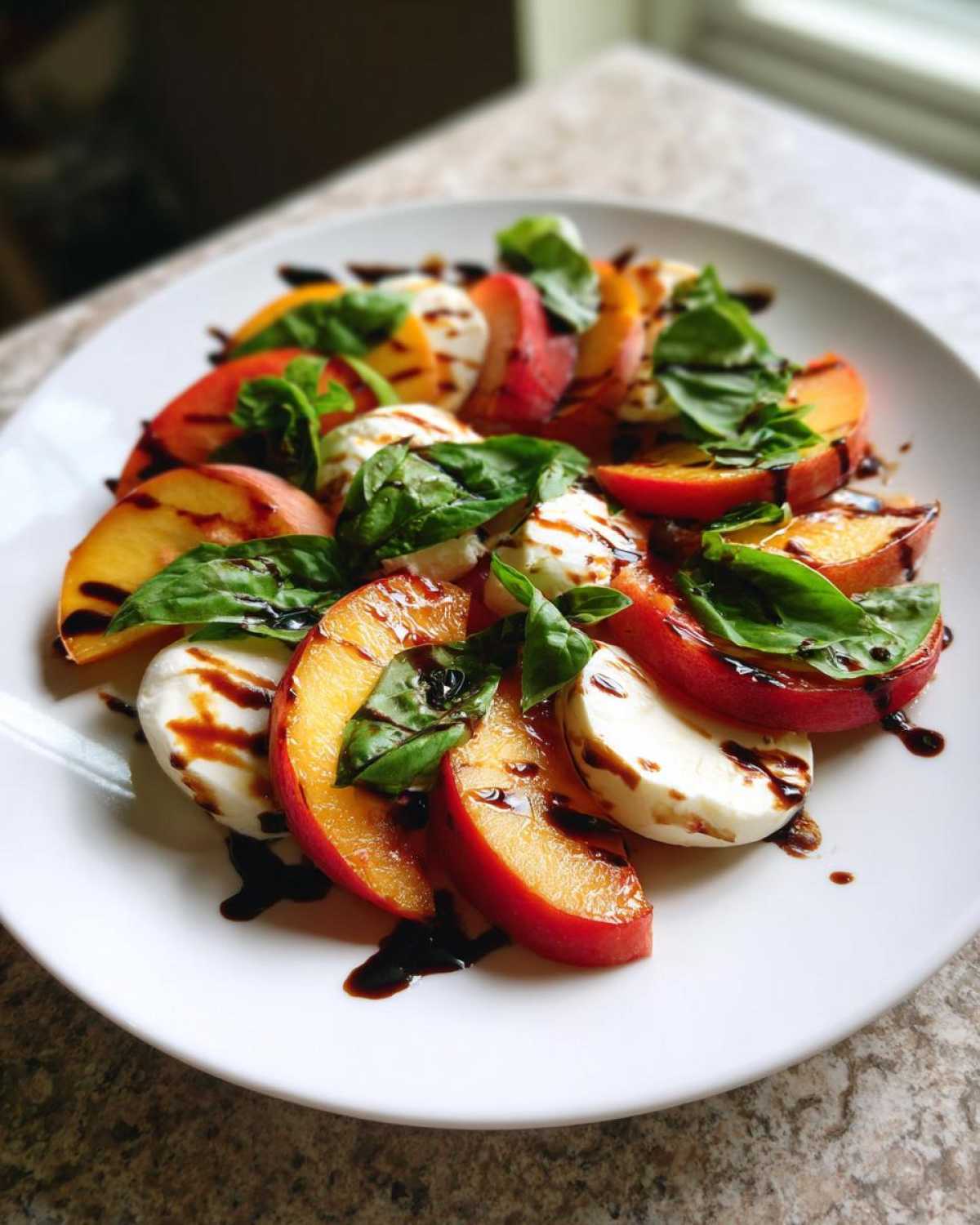 A vibrant Stone Fruit Caprese Salad featuring sliced peaches, fresh mozzarella, and basil drizzled with balsamic glaze.