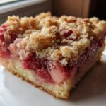 Close-up of a square slice of Strawberry Rhubarb Buckle with Ginger Crumb topping on a white plate.