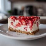 A close-up of a thick slice of Strawberry Rhubarb Cottage Cheese Cake on a white plate.