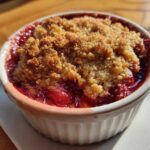 Close-up of a freshly baked Strawberry Rhubarb Crisp bubbling in a white ramekin with a golden brown topping.